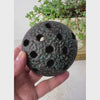 Vintage Japanese ceramic flower frog shown being held and rotated to show the dark brown-black surface, textured domed top, and underside.
