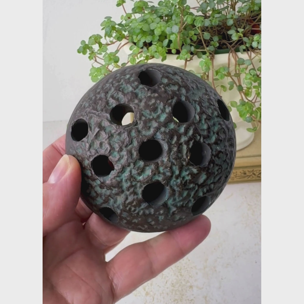 Vintage Japanese ceramic flower frog shown being held and rotated to show the dark brown-black surface, textured domed top, and underside.