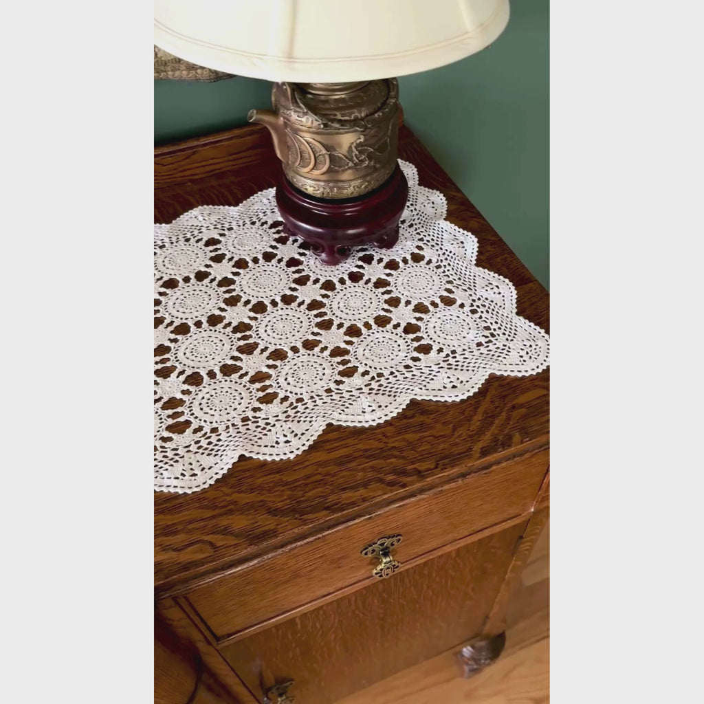 Video of white crochet table runner styled across a wood sideboard with brass candlesticks and a white planter, showing the medallion pattern and scalloped edge.