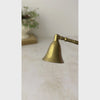 Vintage brass candle snuffer with wood handle shown against a neutral backdrop being displayed close up