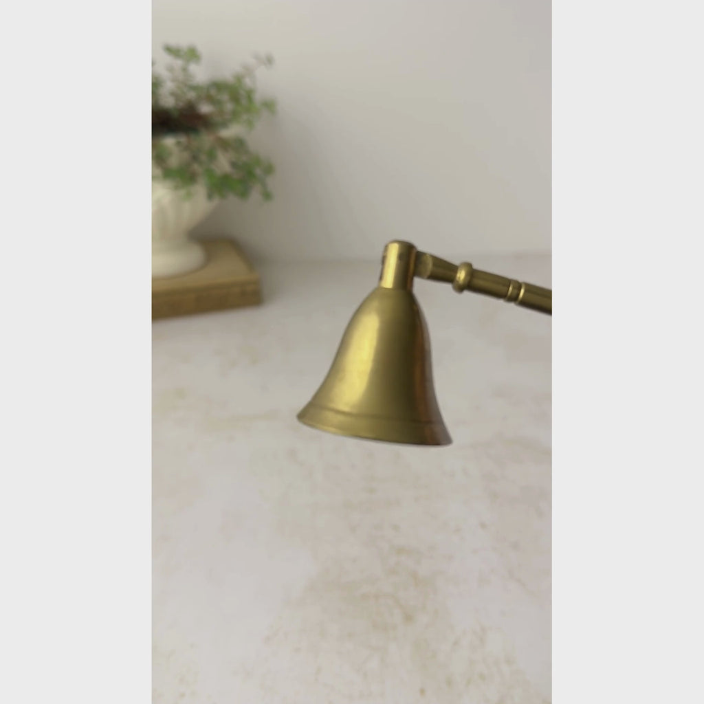 Vintage brass candle snuffer with wood handle shown against a neutral backdrop being displayed close up