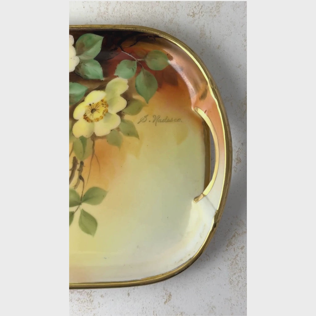 Overhead view of antique porcelain tray shown from the right handle and S. Nadesco signature across the hand-painted florals and gold trim to the left handle.
