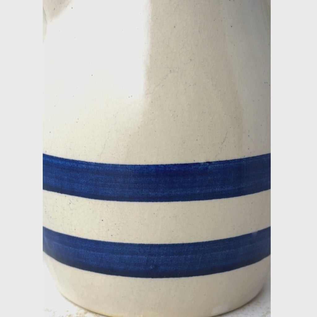 Vintage beige stoneware pitcher shown close-up from the two cobalt blue bands up to the pouring spout and loop handle and back to the blue bands