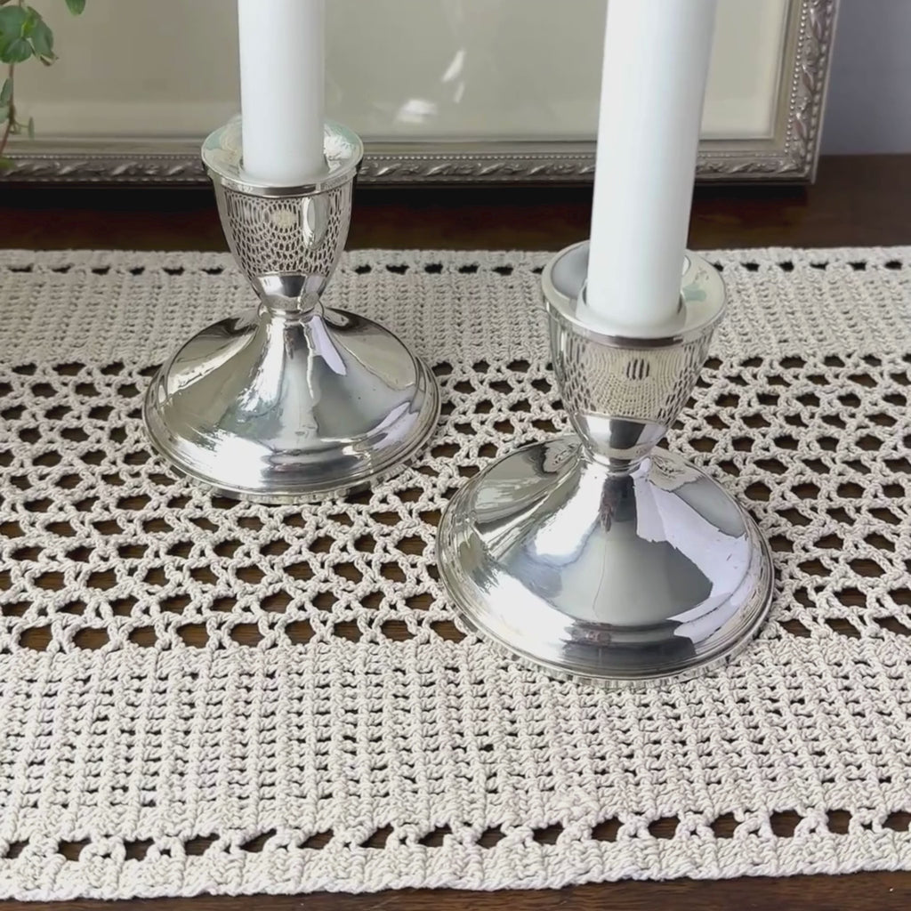 Close-up video of pair of polished sterling silver Duchin candlesticks with wide circular bases and cup-shaped candle sockets on a crochet surface.
